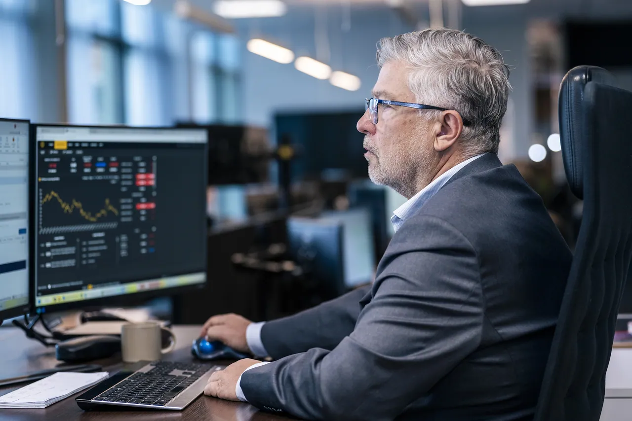 Senior colleague at his desk studying market charts across several screens